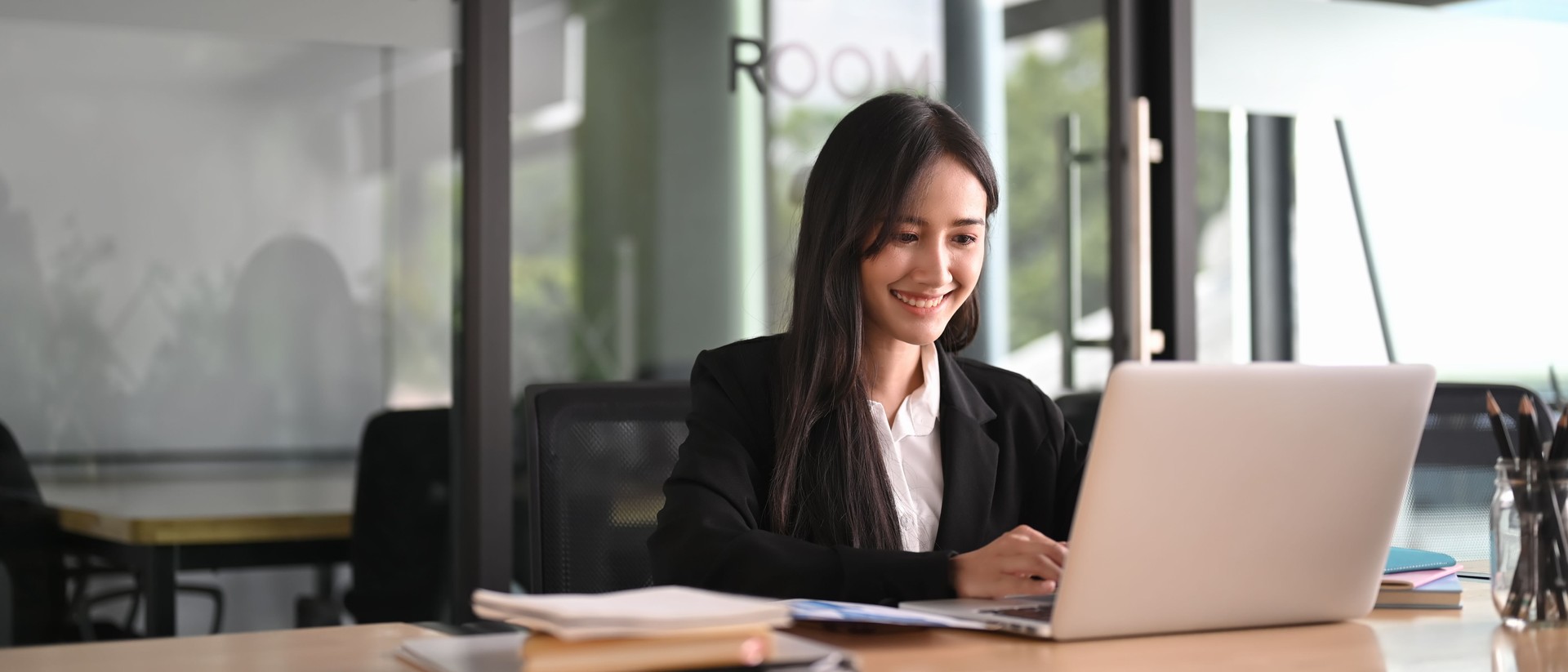 A businesswoman is using a computer laptop while sitting at the wooden working table.